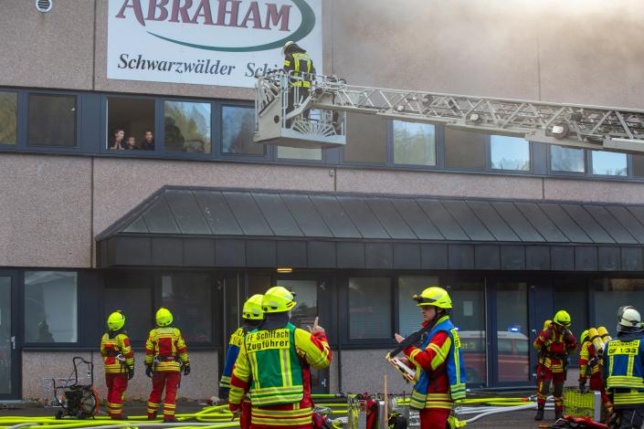 Zug-und Gruppenführer besprechen sich im Vordergrung, während im Hintergrund eine Drehleiter jugendliche aus dem Obergeschoss rettet